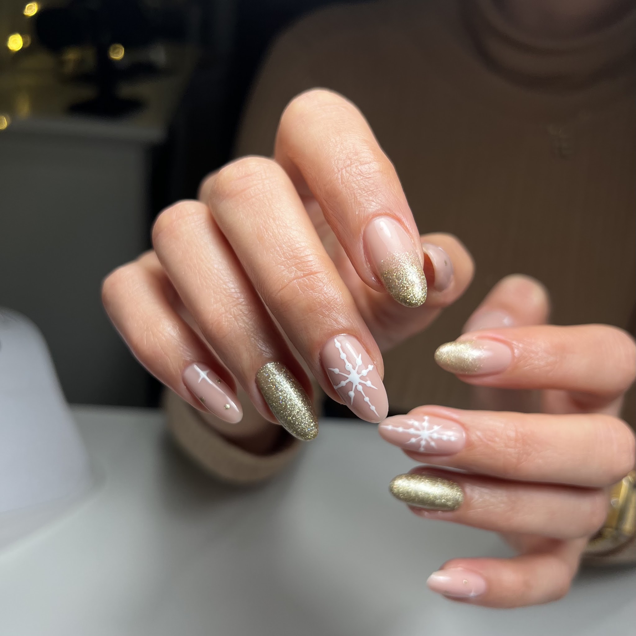 Nude amandelvormige nagels met goudglitter en een handgetekende sneeuwvlok