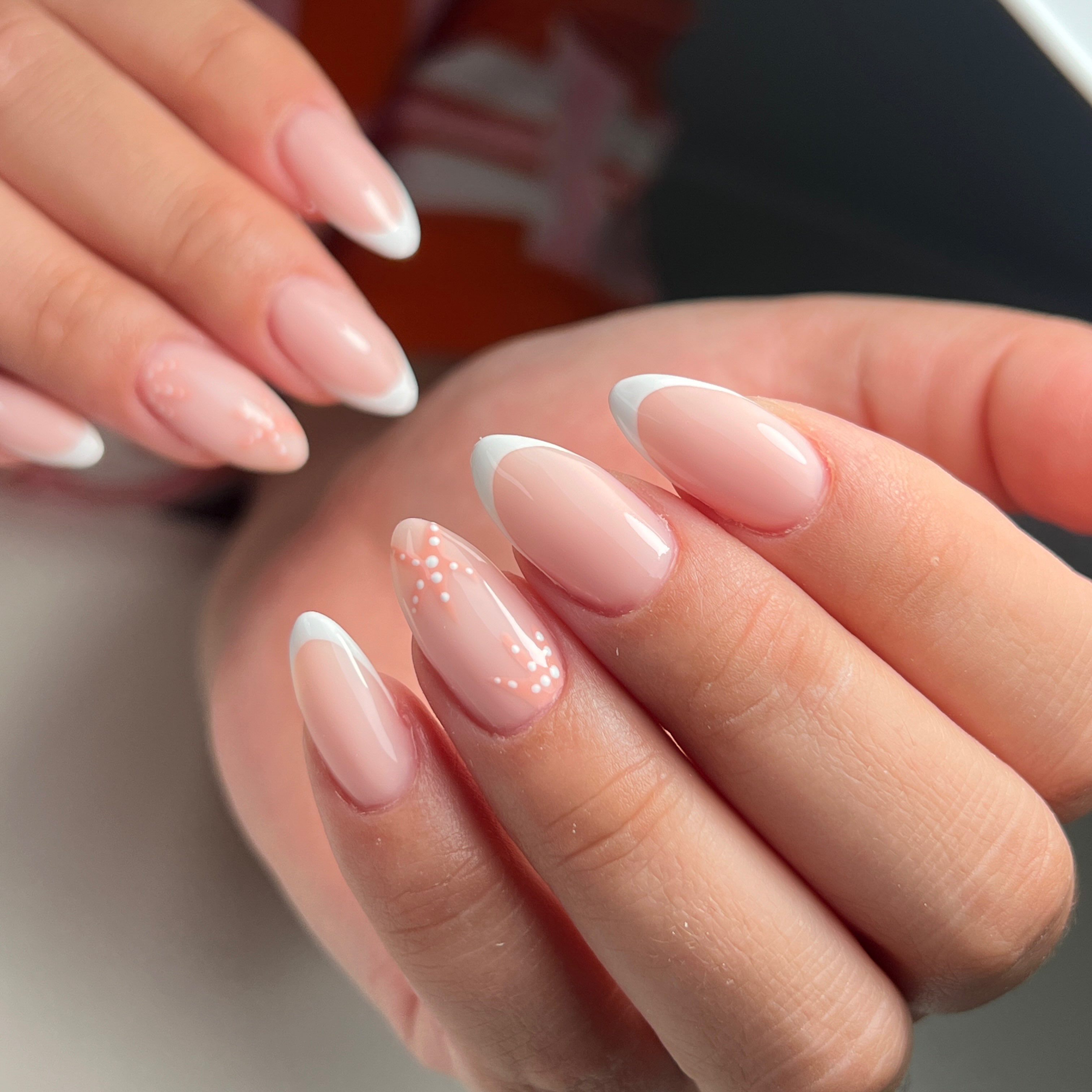 Amandelvormige nagels met witte french tips en een klein accent van stipjes, gezet bij The Nailbar