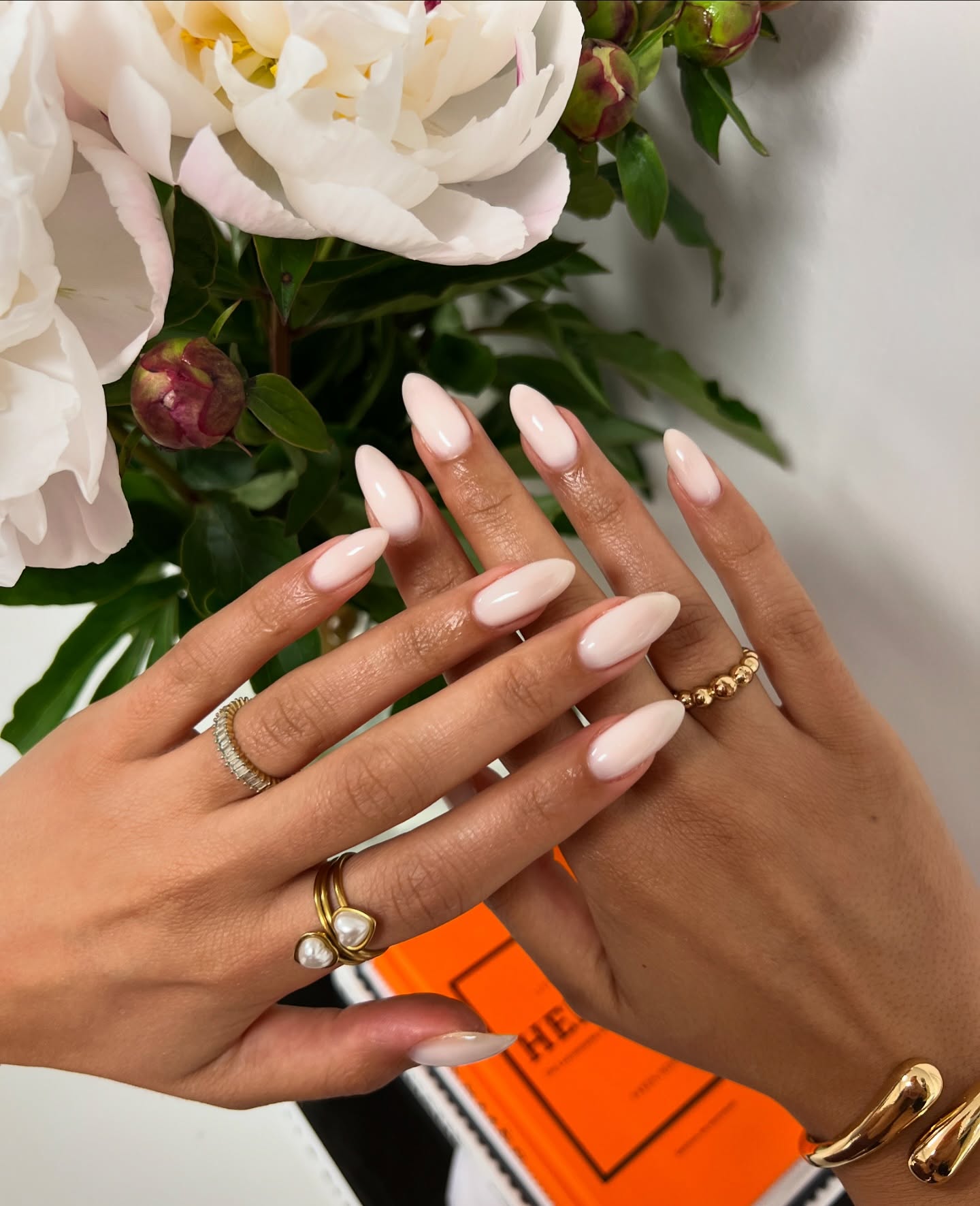 Melkwitte amandelvormige nagels, in de hand met gouden ringen voor witte pioenrozen